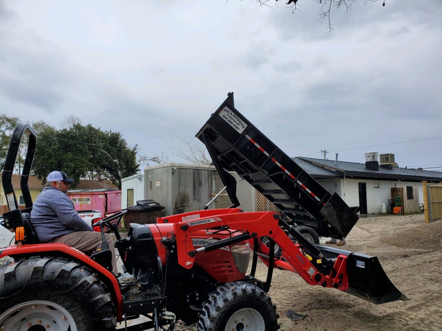 A man on a tractor with a dump truck in the background.