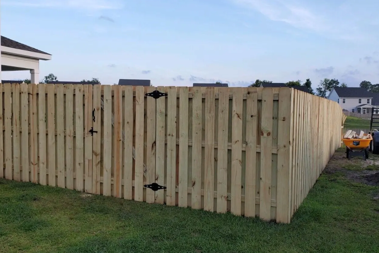 A wooden fence with two black diamond shaped hinges.